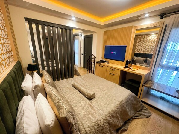 A modern hotel room with a large bed, a desk with a computer, a TV, and a glass partition. - DATÇA SUİTES LUXURY BOUTİQUE HOTELS (Datça)