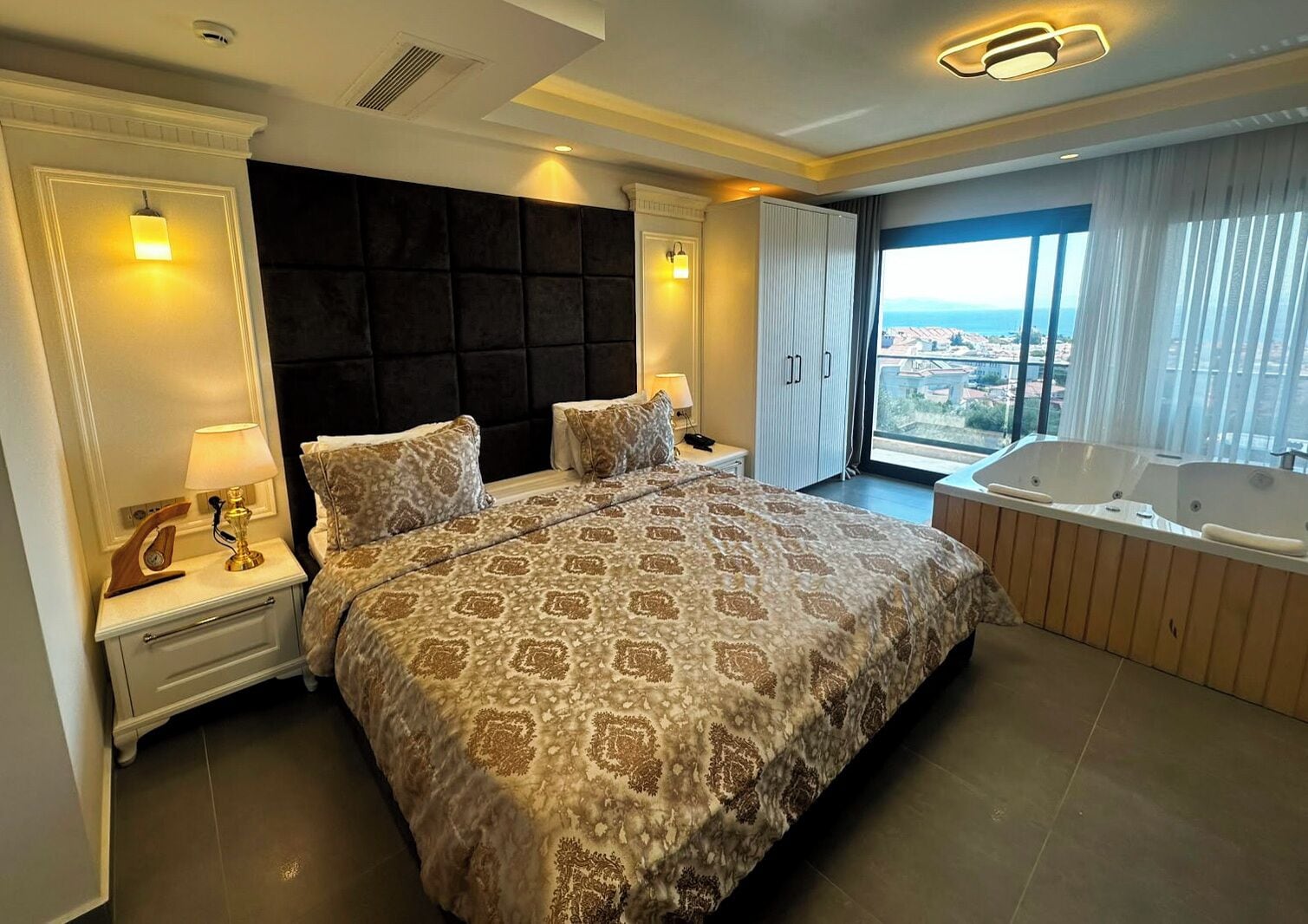 Un dormitorio amplio con una cama grande, un baño privado con jacuzzi y vistas a la ciudad.