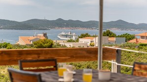 Vista al mar con un crucero, bancos de madera y una mesa con bebidas.