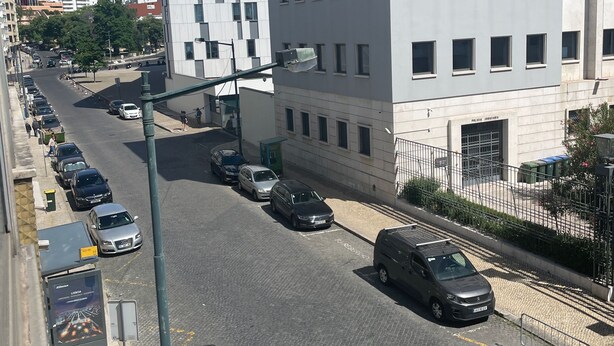 Een modern gebouw met een gevel in rastervorm, een verharde straat met geparkeerde auto's, en een helderblauwe lucht.