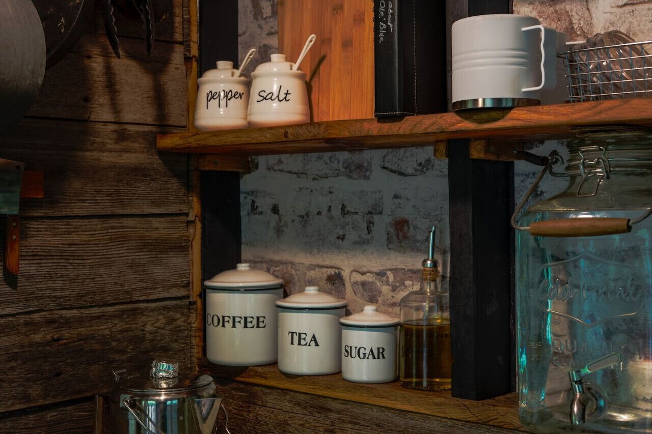 En køkkenhylde med mærkede beholdere til kaffe, te, sukker, peber og salt.