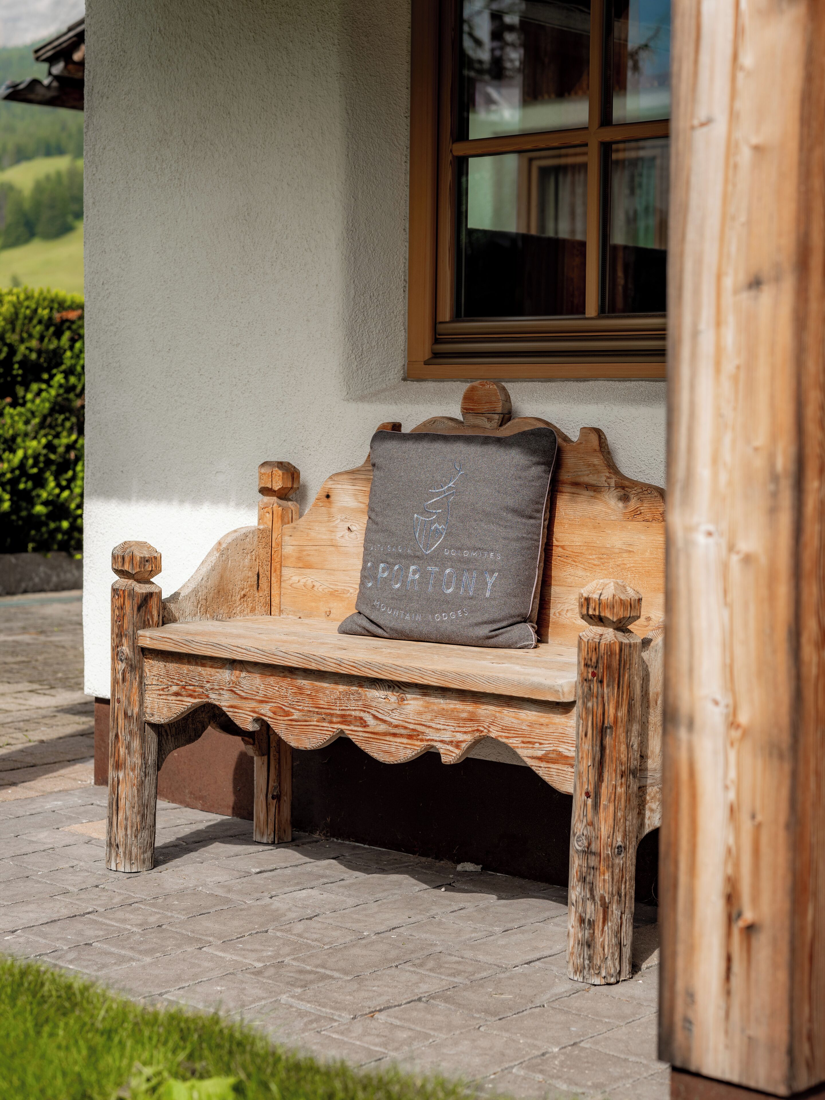 A wooden bench with a cushion, positioned outside a building with a window.