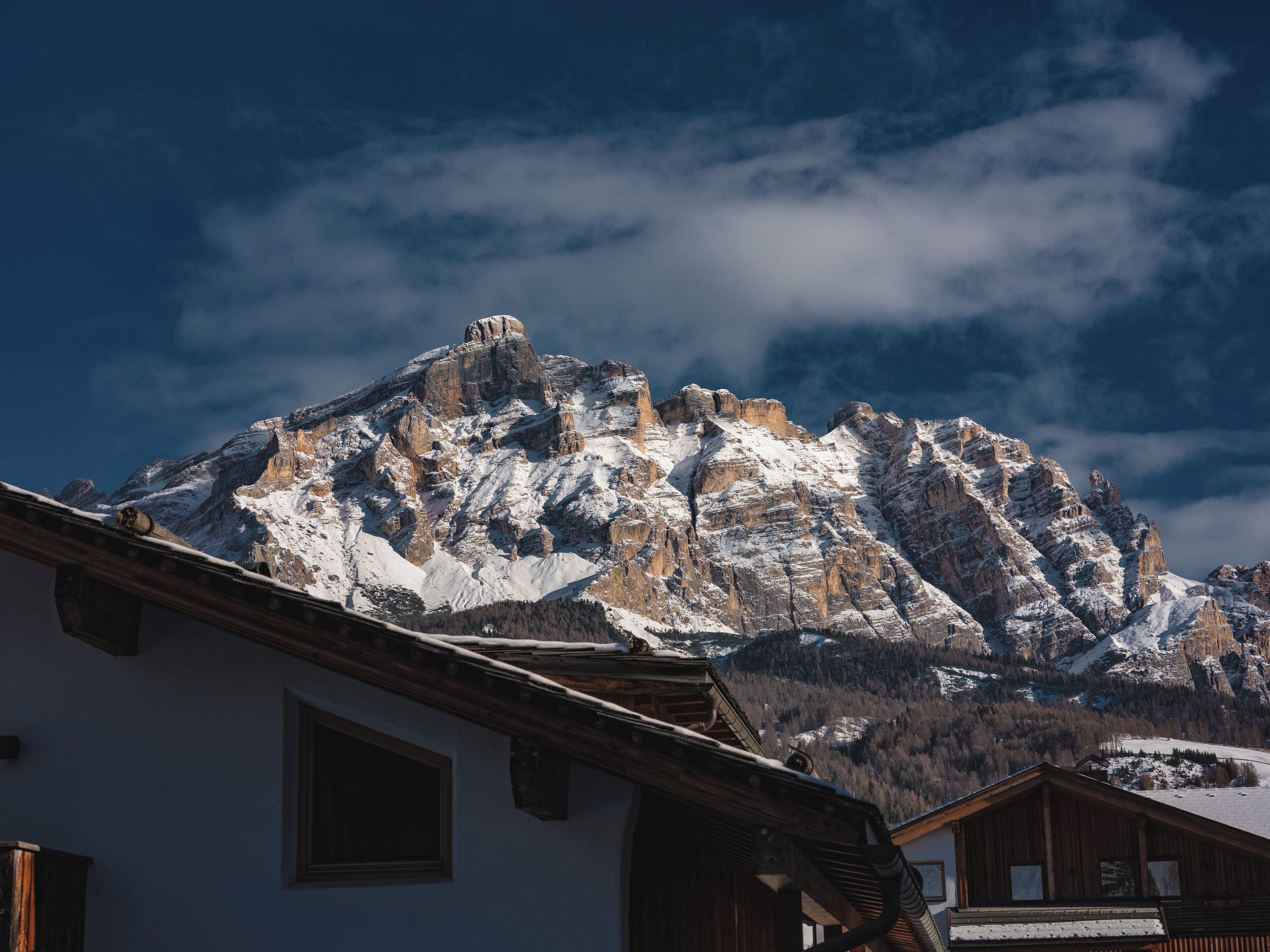 Una montaña con picos nevados y un edificio de madera con techo inclinado en primer plano.