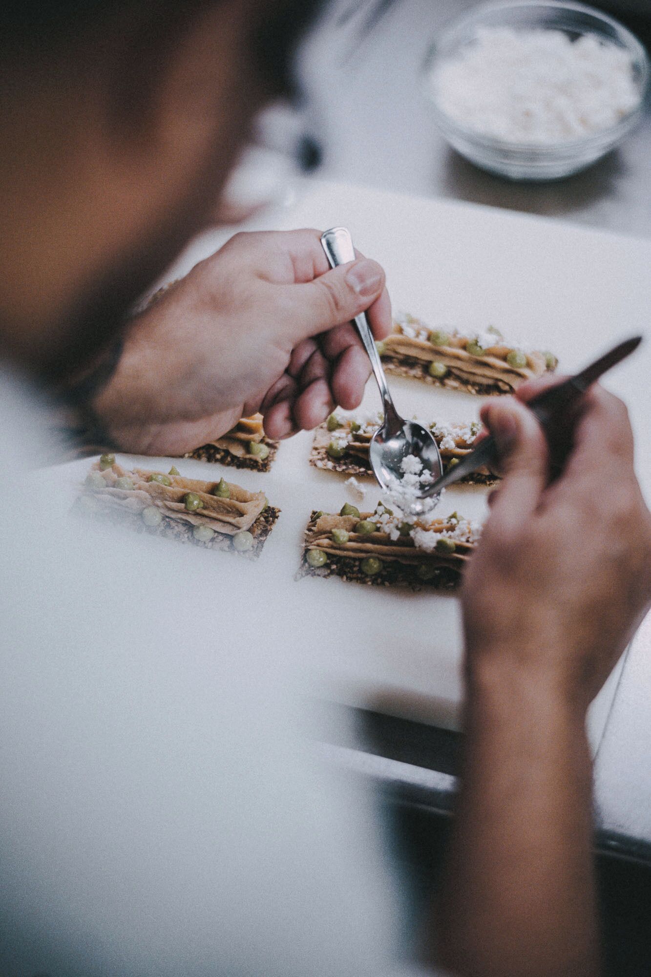 A person preparing food with a spoon and a knife on a white surface.