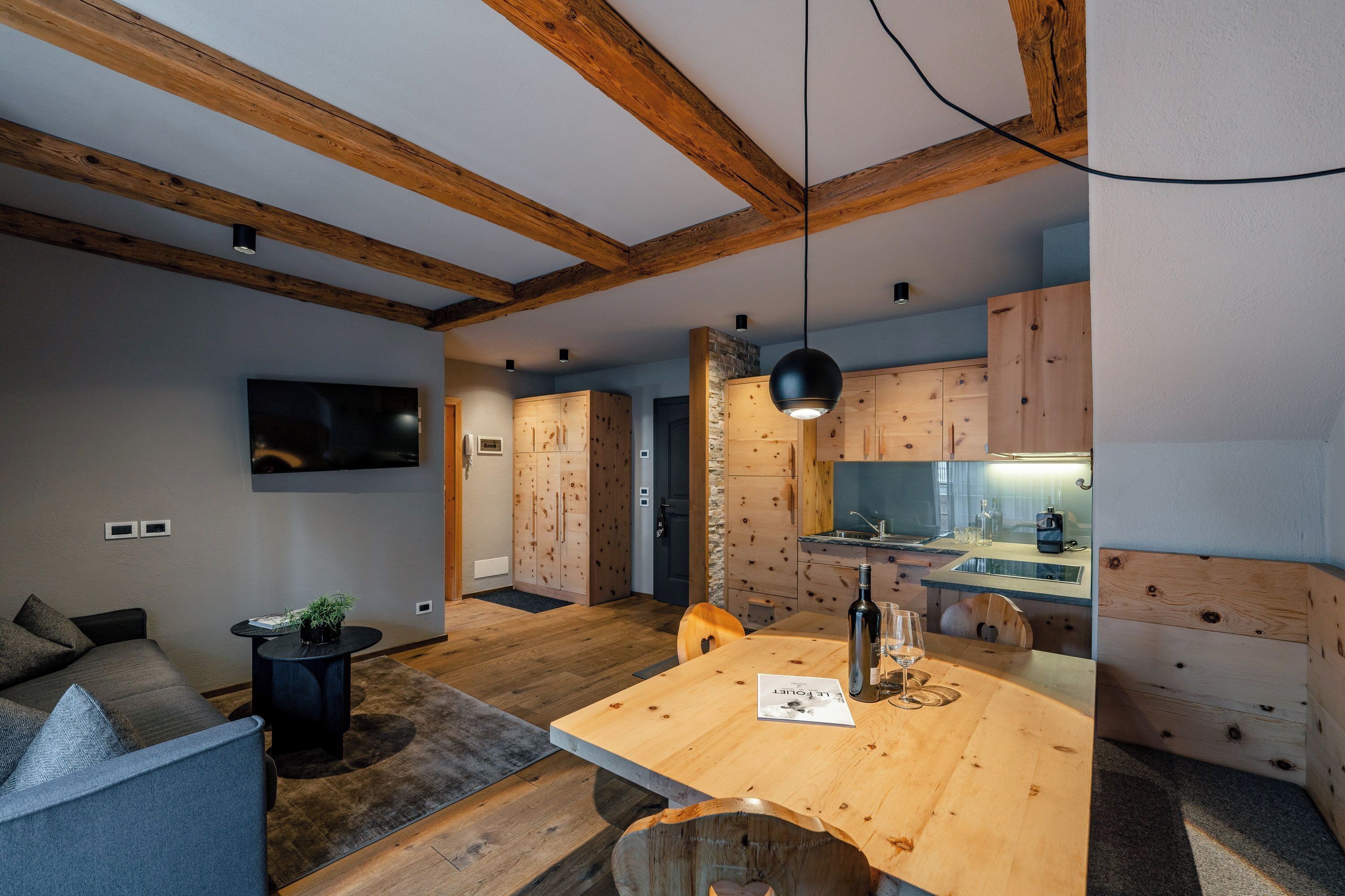 A modern kitchen with wooden cabinets, a dining table, and a TV mounted on the wall.