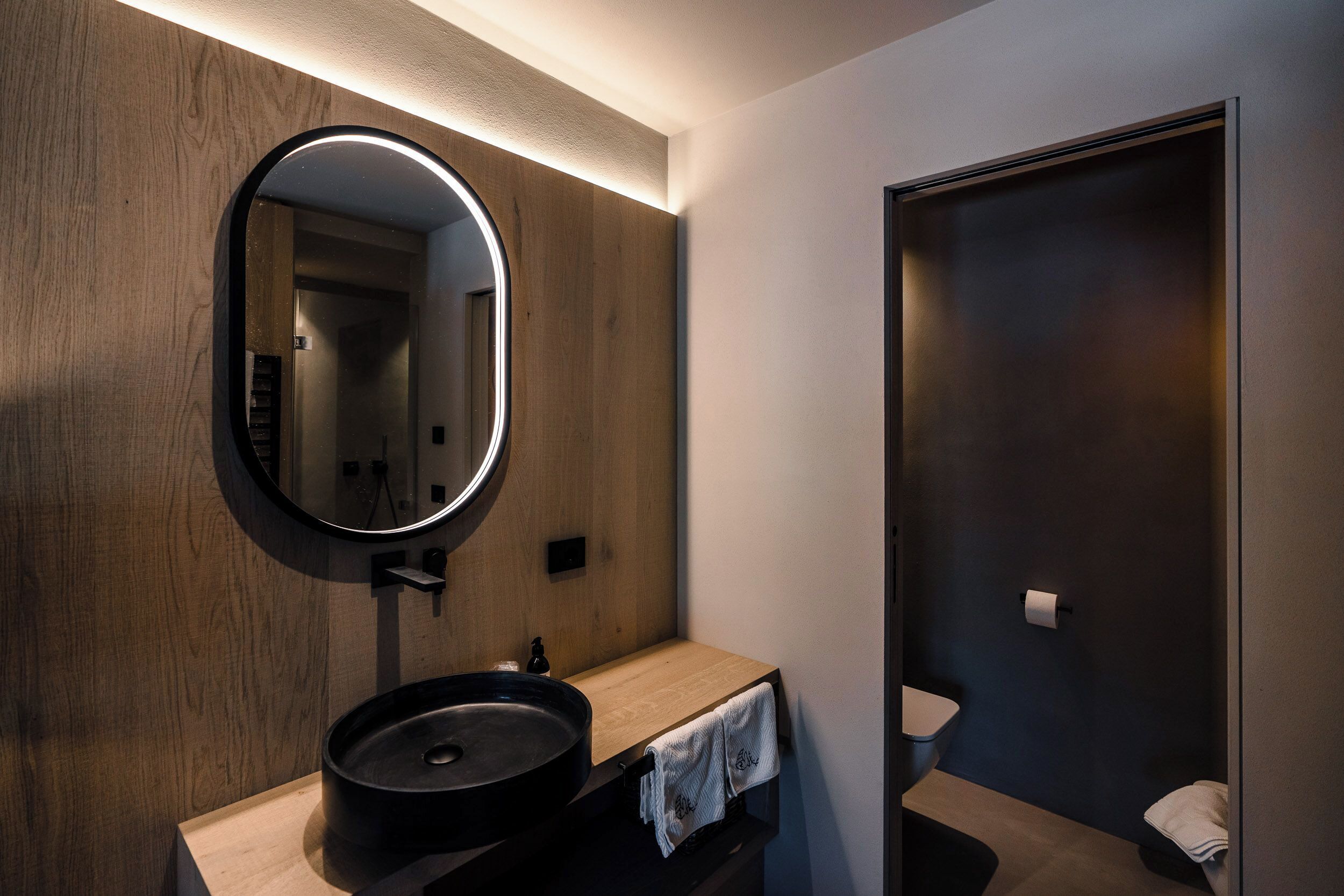A modern bathroom with a wooden vanity, a round mirror, and a dark-colored sink.