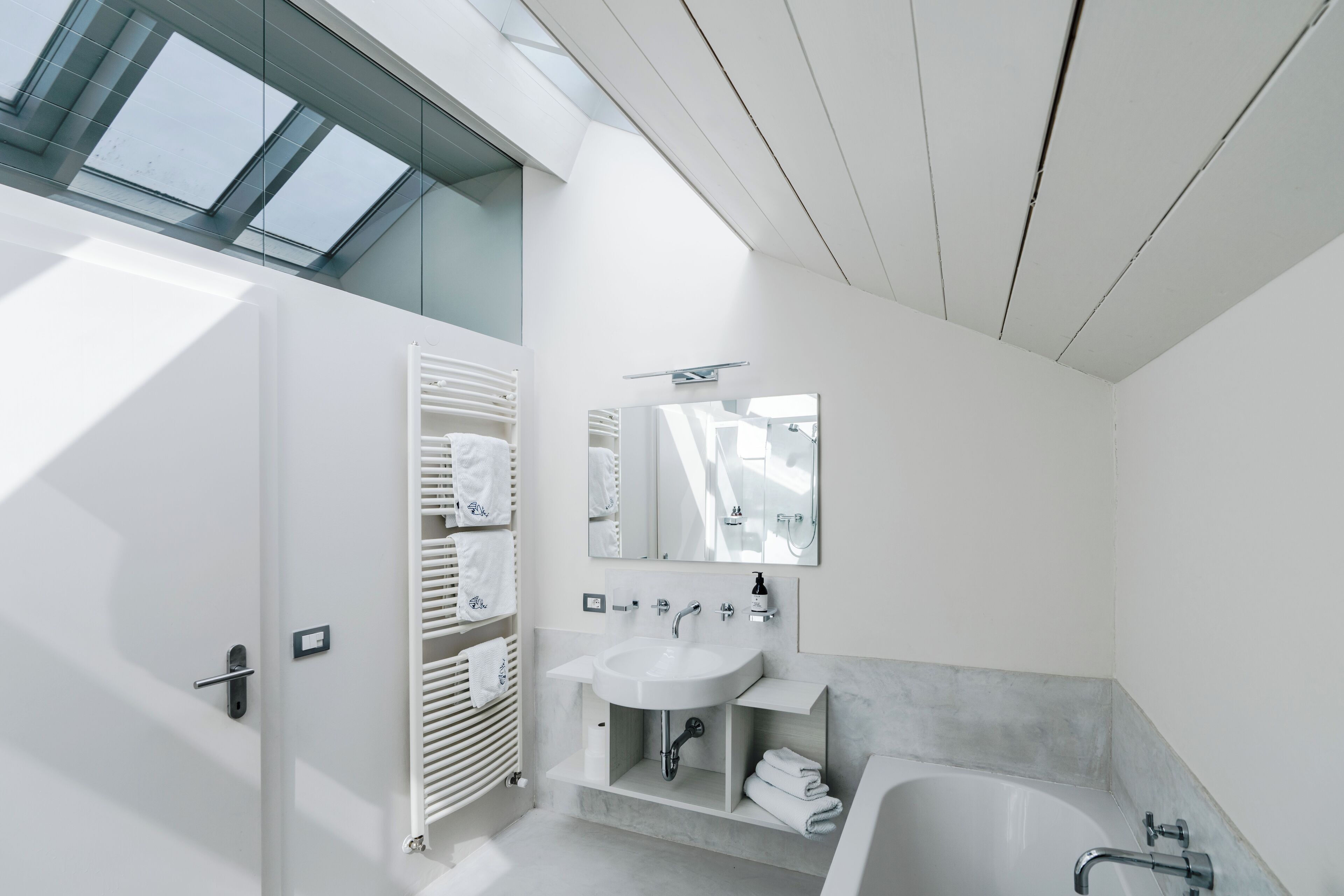 A modern bathroom with a skylight, a white sink, a bathtub, and a towel rack.