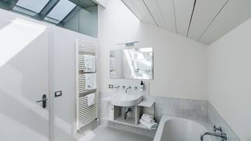 A modern bathroom with a skylight, a white sink, a bathtub, and a towel rack.