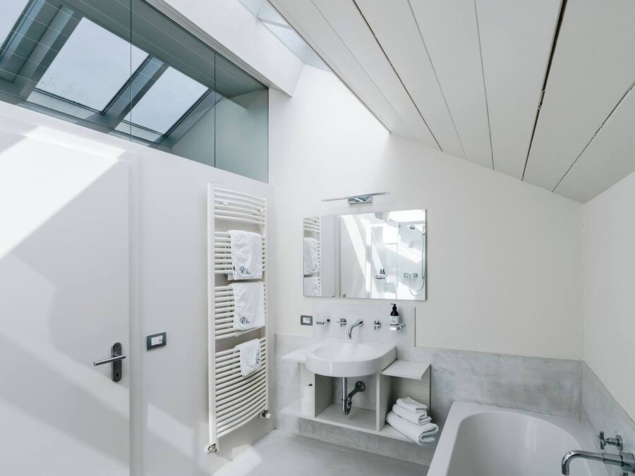 A modern bathroom with a skylight, a white sink, a bathtub, and a towel rack.