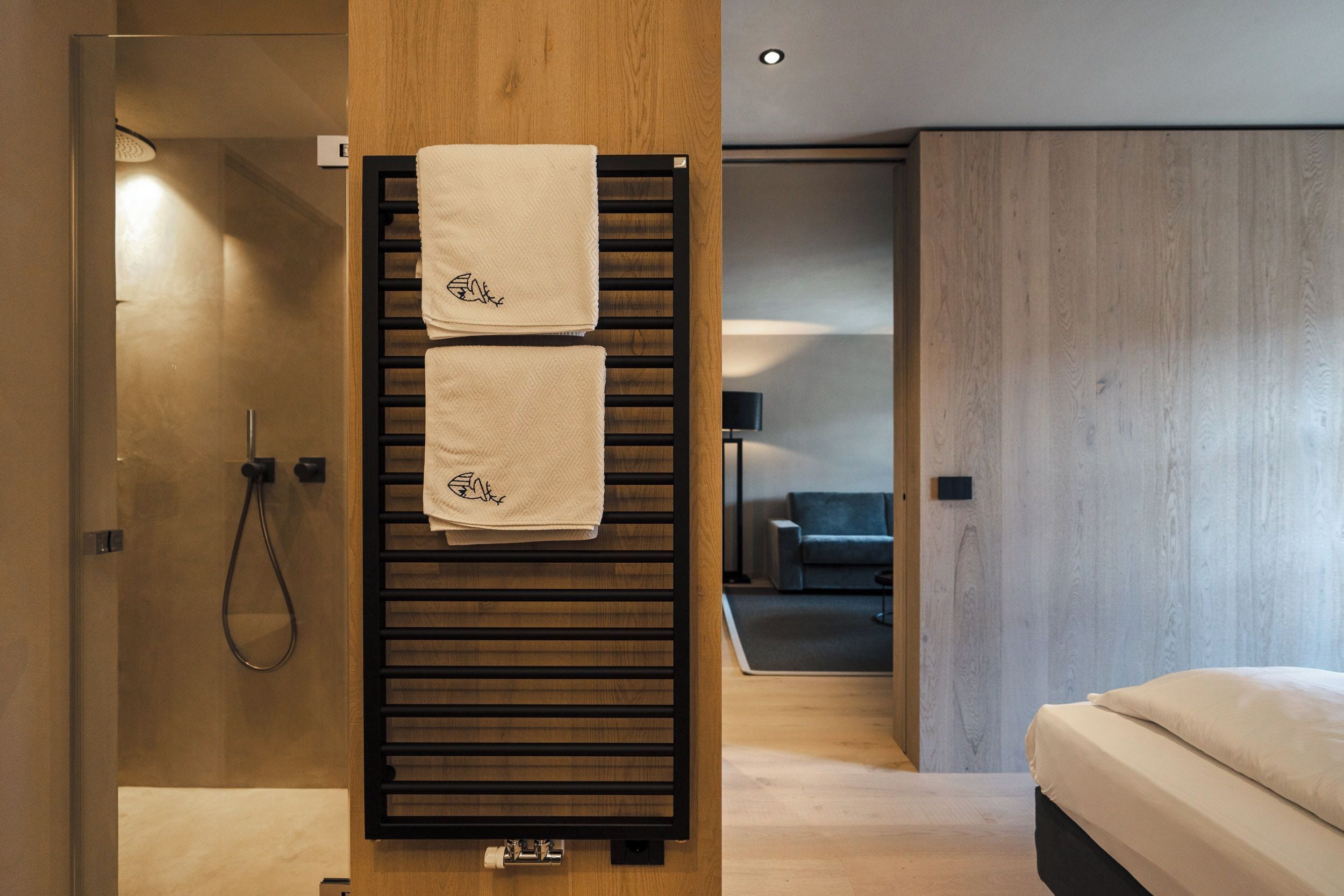 A modern bathroom with a wooden towel rack holding two towels, a glass shower enclosure, and a visible toilet.