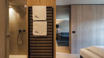 A modern bathroom with a wooden towel rack holding two towels, a glass shower enclosure, and a visible toilet.