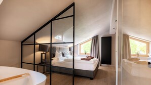 Un dormitorio moderno con techo inclinado, una cama grande, una mesita de noche con lámpara y vistas al exterior.