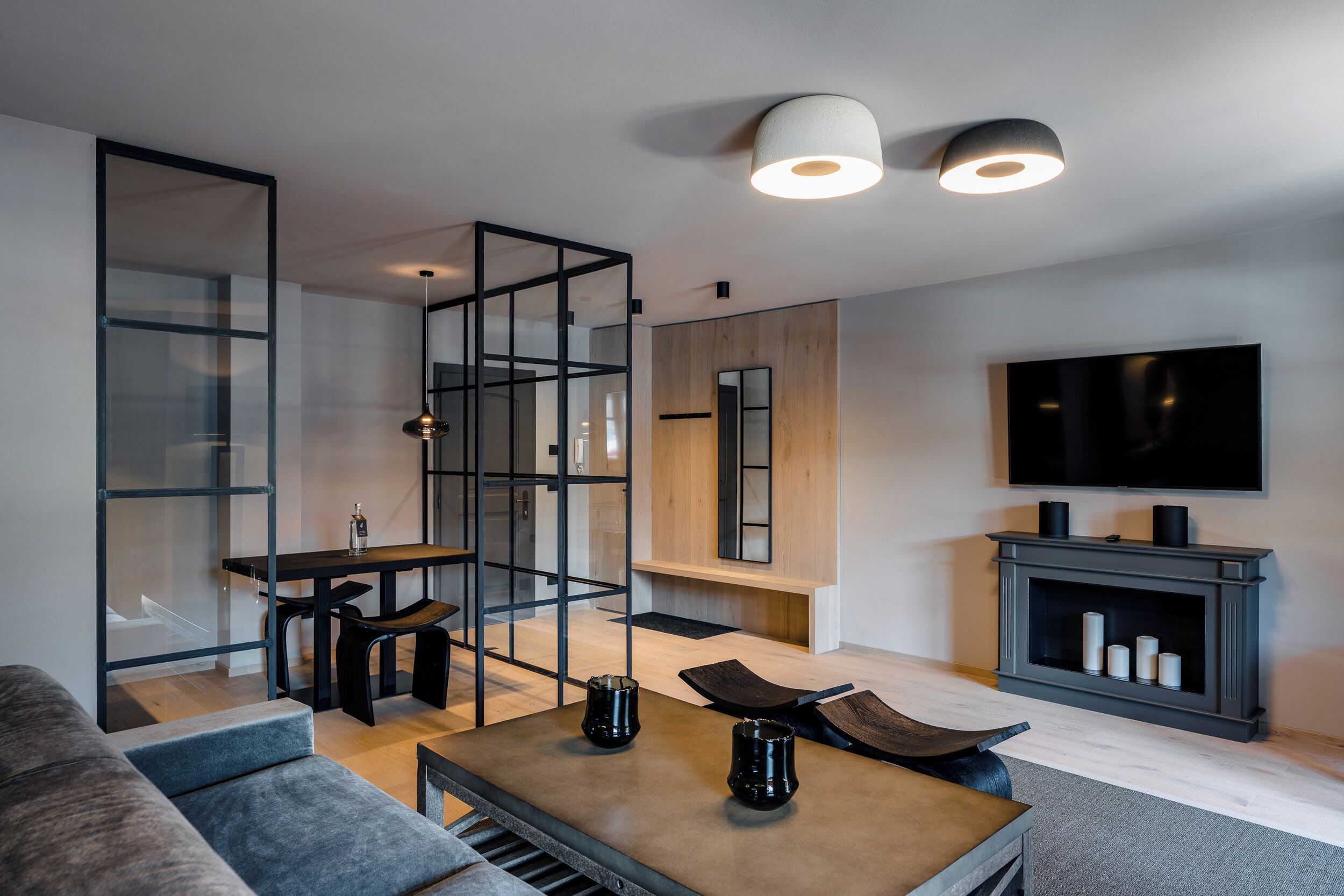 Een moderne woonkamer met een glazen scheidingswand, een houten eettafel, een bank, een salontafel en een open haard.