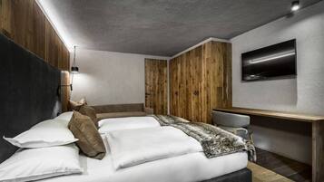 A modern bedroom with a large bed, a desk, and a TV mounted on the wall.