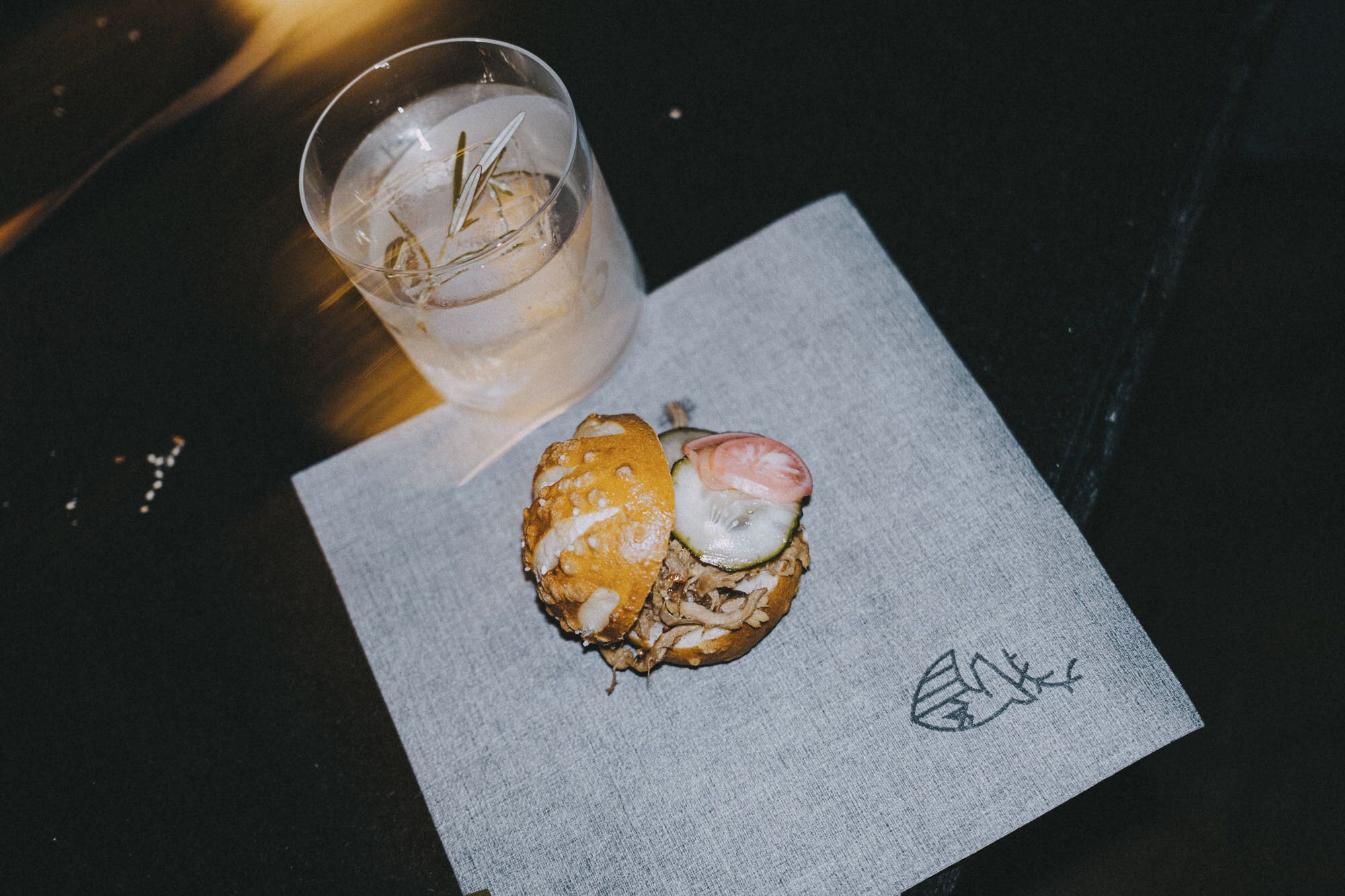 Ein Sandwich mit Tomatenscheibe und ein Getränk im Glas auf einem Servietttuch.