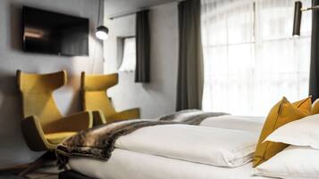 A hotel room with a bed, two yellow chairs, a flat-screen TV, and a large window with curtains.