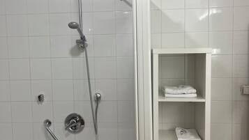 Een moderne badkamer met een bad, een douche met een handdouche en een betegelde muur. Er is een wit plankje met handdoeken en een mandje.