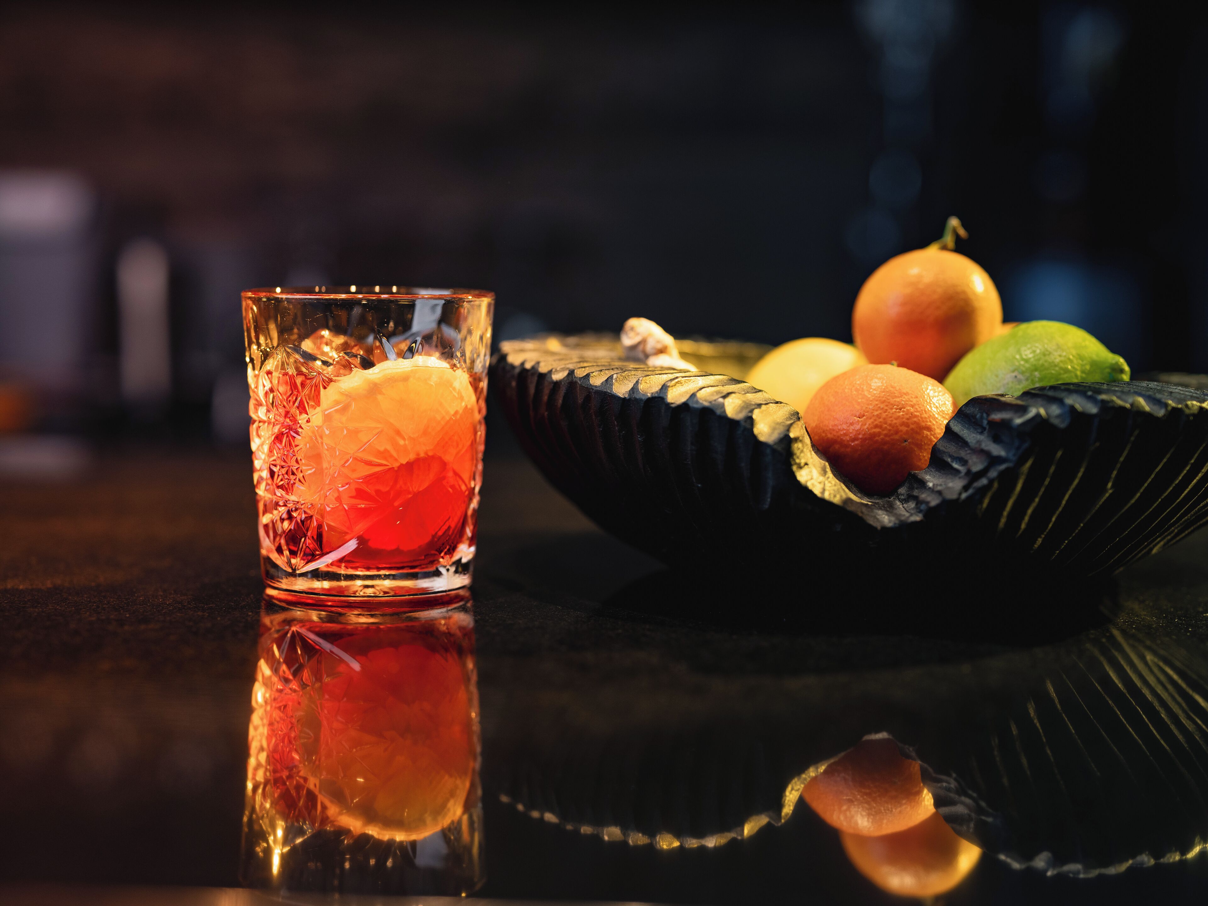 A glass with a clear liquid and a slice of orange, placed on a reflective surface.