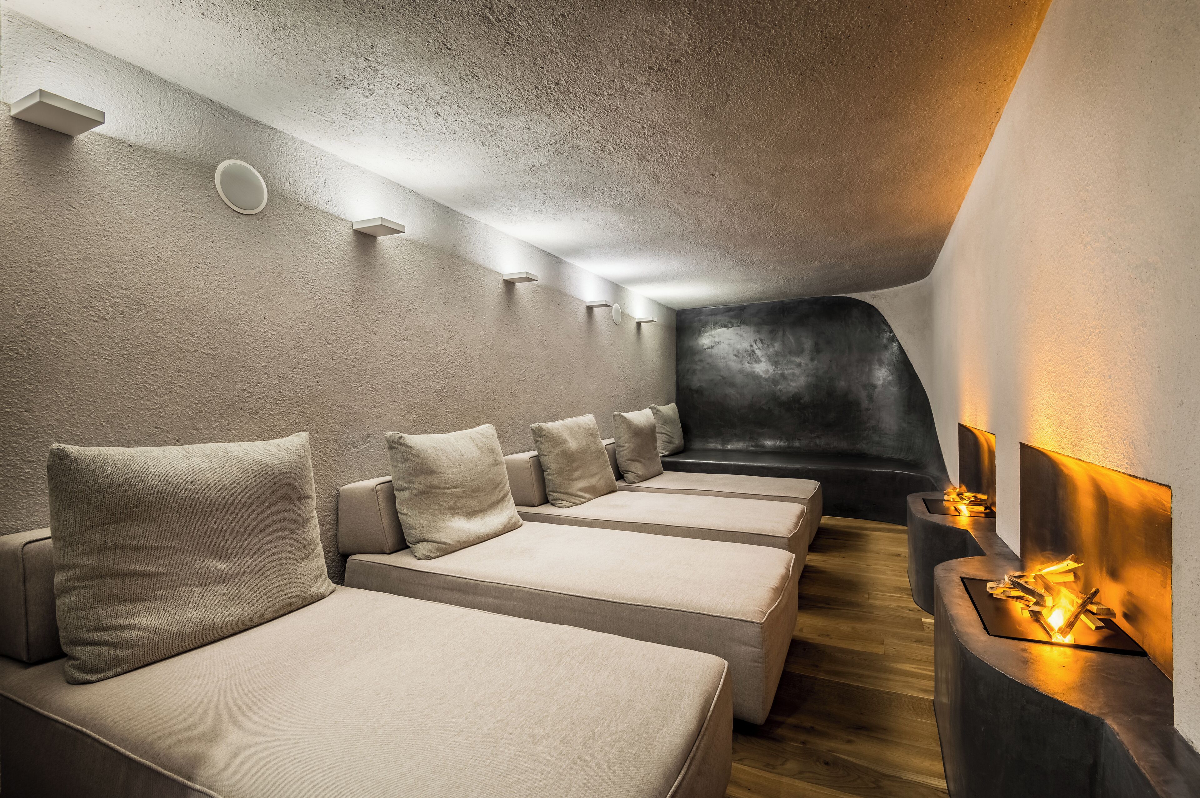 A modern spa room with multiple massage tables, a dark wall feature, and a wall-mounted fireplace.