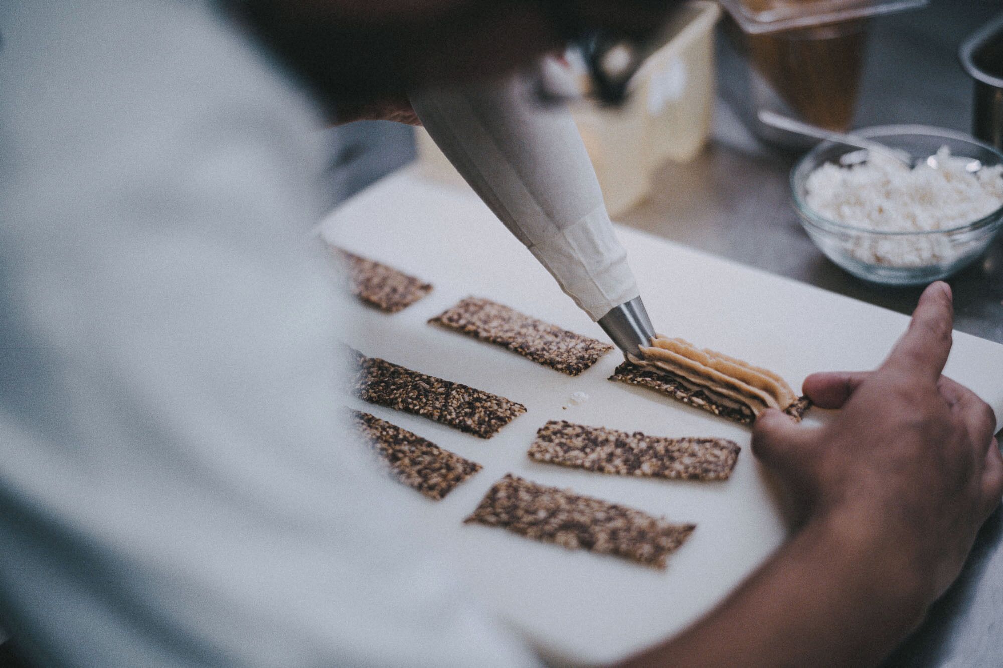 A person preparing food, specifically spreading a mixture on a cutting board with several pieces of bread.