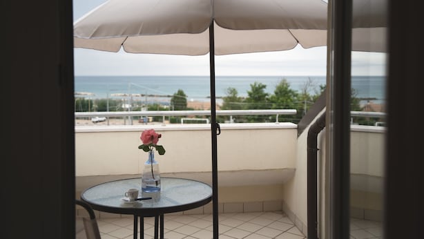 Un balcon avec une table, un parasol blanc et un vase contenant une fleur rose.