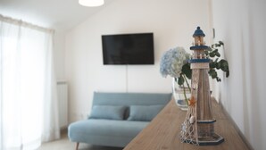 Une table en bois surmontée d’une maquette de phare décorative, un canapé bleu et un téléviseur fixé au mur dans un salon moderne.