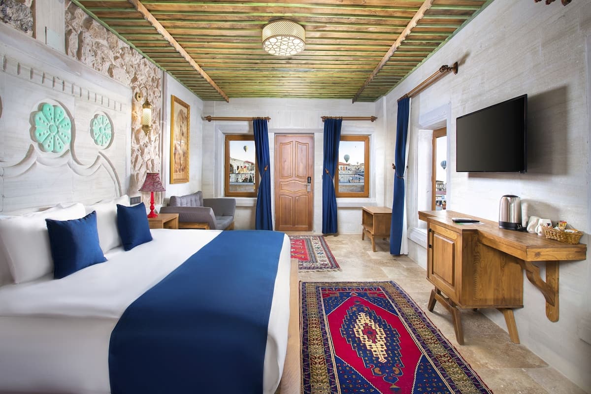 Une chambre d’hôtel avec un grand lit, un bureau en bois, une télévision et une vue sur la ville par la fenêtre.