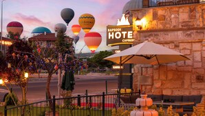 A hotel with a stone facade, outdoor seating, and a view of hot air balloons. - Rapsodi Cappadocia (Çavuşin)