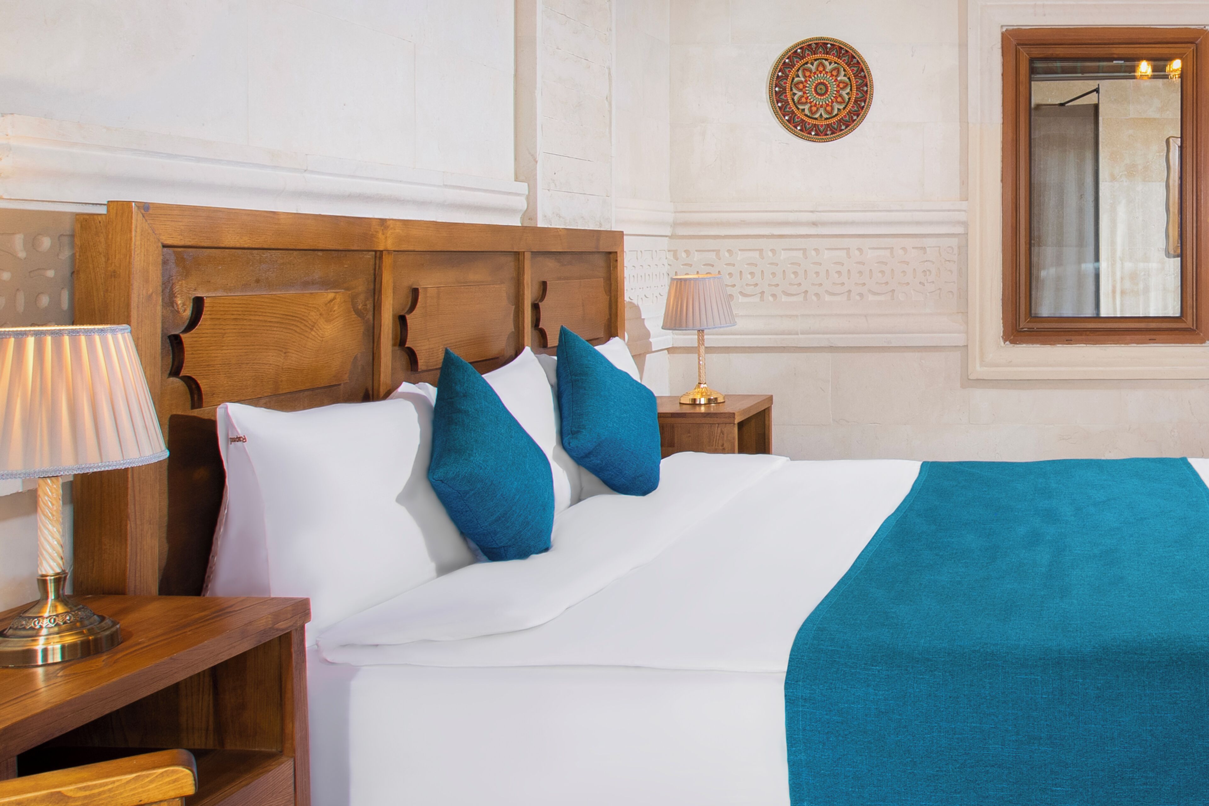 A neatly made bed with a wooden headboard, a teal throw blanket, and two blue pillows.