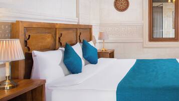 A neatly made bed with a wooden headboard, a teal throw blanket, and two blue pillows.