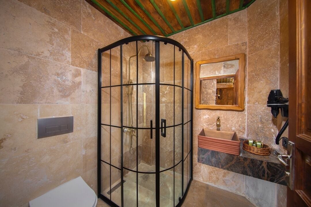 Casa de banho com chuveiro em cabine de vidro, lavatório de mármore e espelho com moldura de madeira.