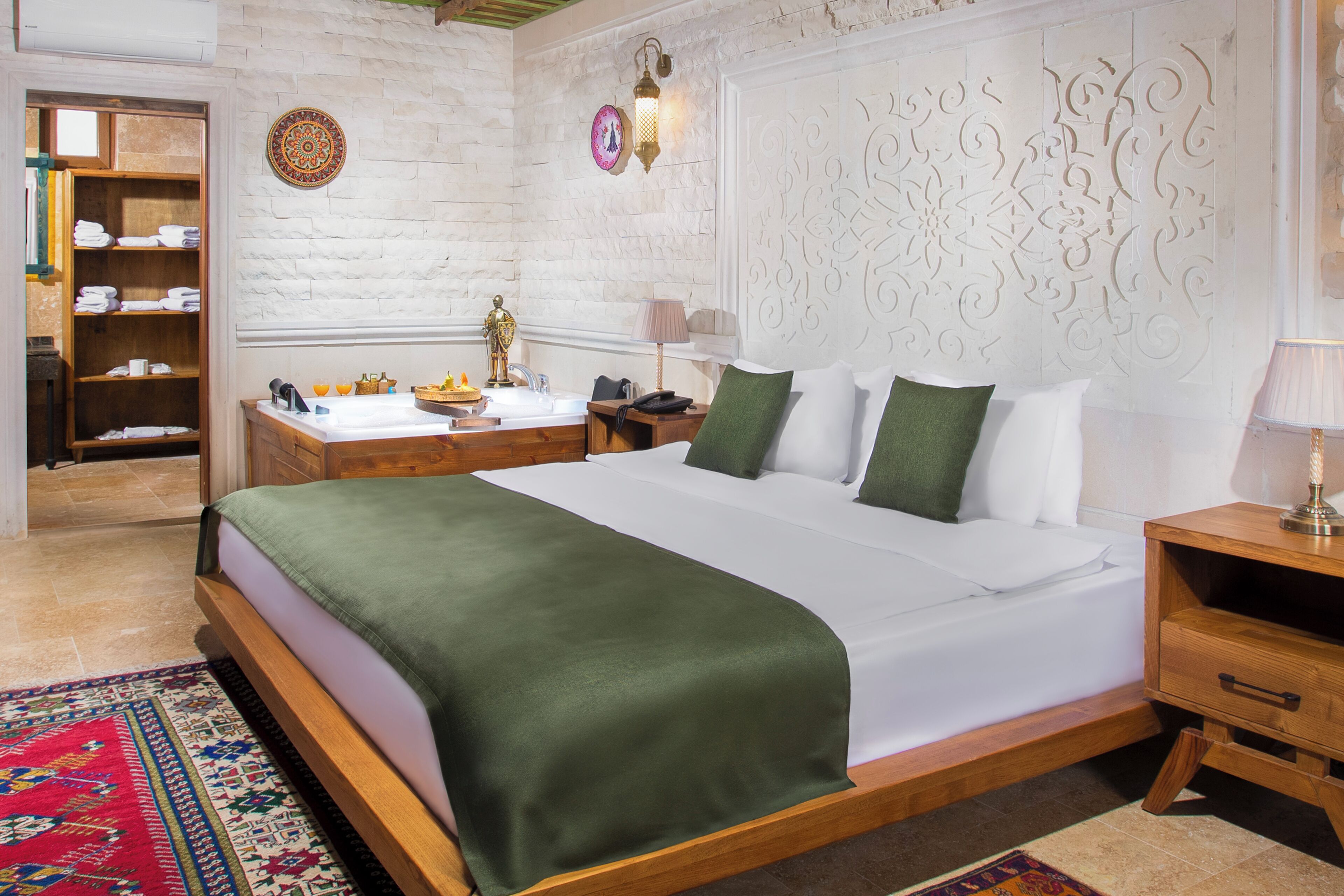 A neatly arranged bedroom with a large bed, a wooden nightstand, a bedside table, and a built-in shelf with folded towels.