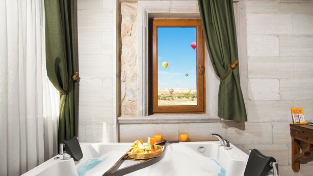 Un baño con bañera, ventana con vistas a globos aerostáticos y una mesita de madera con una cesta de fruta.