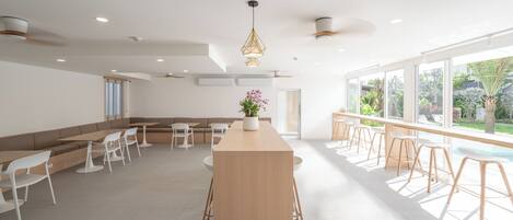 Un comedor moderno y bien iluminado con una barra de madera central, sillas blancas y un amplio ventanal con vistas al exterior.