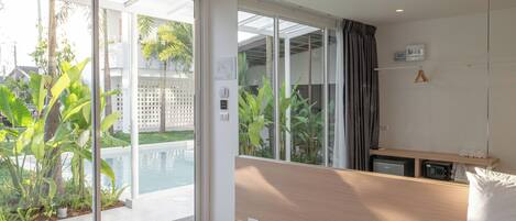 Habitación de hotel moderna con una cama grande, un escritorio pequeño y vistas a una piscina y vegetación exterior.