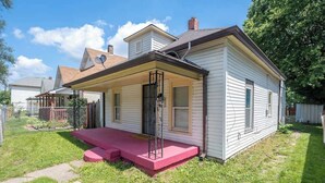A single-story house with a front porch, a small attached garage, and a fenced backyard. - Affordable Cozy Retreat in Indianapolis (Indianapolis)