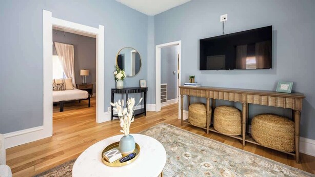 A living room with a TV mounted on the wall, a round coffee table with a vase and remote, and a console table with baskets. - Affordable Cozy Retreat in Indianapolis (Indianapolis)