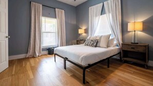 A bedroom with a bed, two bedside tables, a window with curtains, and a lamp on a nightstand. - Affordable Cozy Retreat in Indianapolis (Indianapolis)