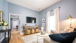 A modern living room with a sofa, a coffee table, a TV mounted on the wall, and a console table with decorative items. - Affordable Cozy Retreat in Indianapolis (Indianapolis)
