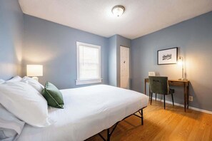 Une chambre à coucher avec un lit, un bureau, une chaise, une fenêtre et une porte.