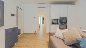 Eine moderne Wohnung mit einer Küchenzeile, einer Couch mit Kissen, einem Holzboden und einem Flur, der in einen anderen Raum führt.