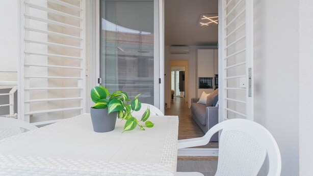 Ein moderner Balkon mit einem weißen Tisch, zwei Kübelpflanzen und einem weißen Stuhl.