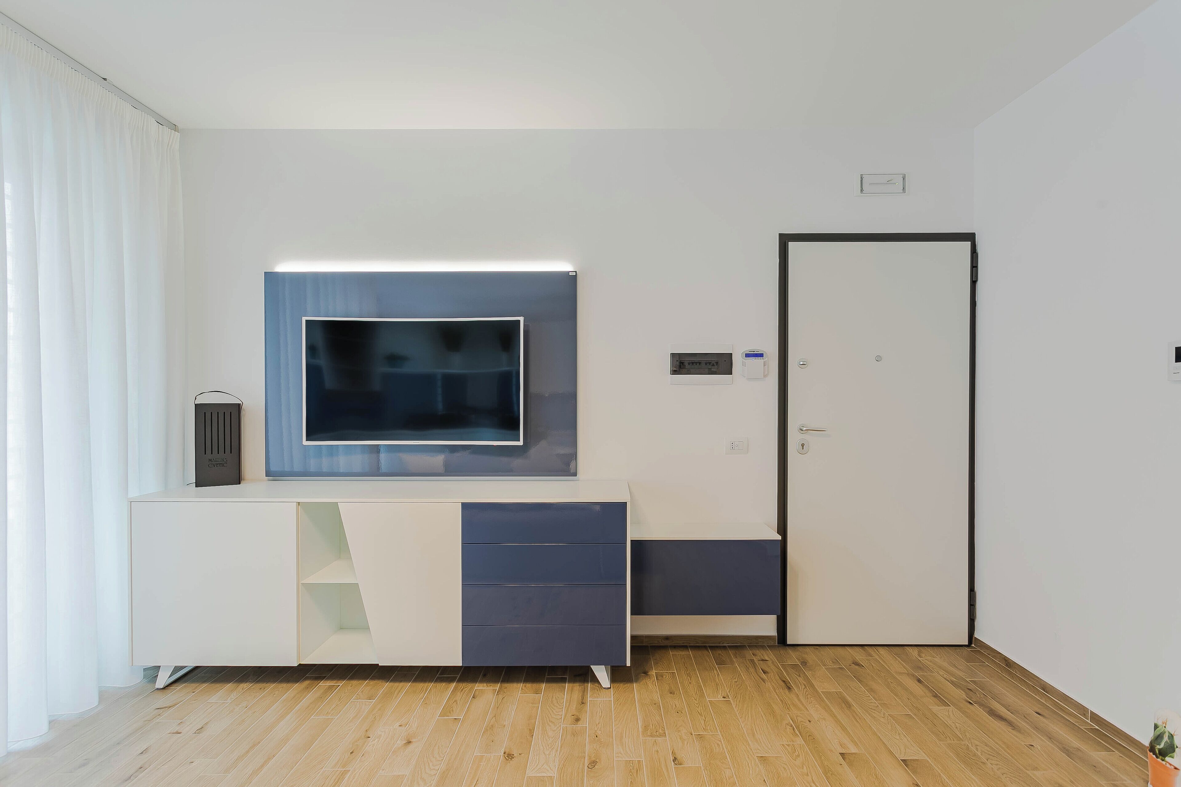 Een moderne kamer met een wit en grijs bureau, een flatscreen-televisie, een deur en een kleine plant.