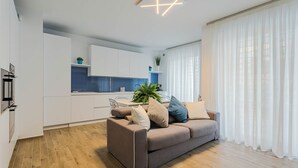 Ein modernes Wohnzimmer mit einem braunen Sofa, einem Essbereich mit blauer Arbeitsplatte und einer Küche im Hintergrund.