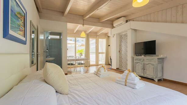 A hotel room with a large bed, a television, a bathroom with a sink, and a view of the outside. - Terrazza Corallo by Wonderful Italy (Bari)