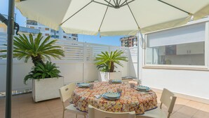 A round table with a patterned tablecloth, surrounded by chairs, under a large umbrella. - Terrazza Corallo by Wonderful Italy (Bari)