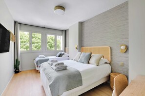 A modern hotel room with a large bed, a smaller bed, and a desk. There is a window with curtains, a flat-screen TV, and a plant. - Résidence MEUDON (Meudon)