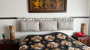 Quarto com cama, cabeceira, barra de cortina e cortinas cinzas, armário de madeira e um quadro decorativo na parede.