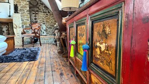 Um interior rústico com pisos de madeira, parede de pedra e um armário vermelho com objetos decorativos.