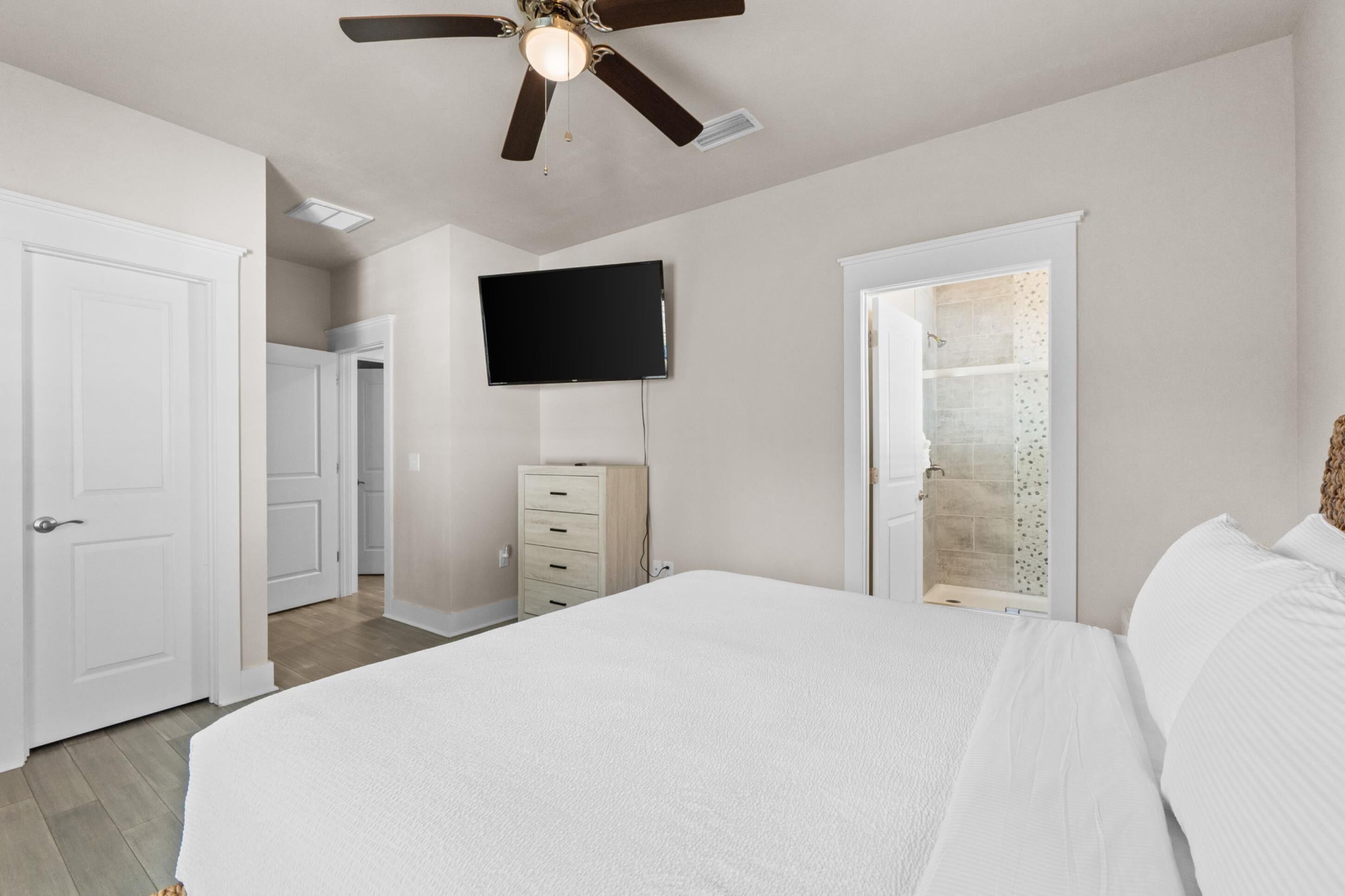 A bedroom with a bed, a ceiling fan, a TV mounted on the wall, and a walk-in closet.